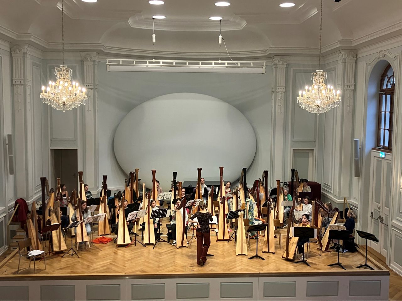 Eine grosse Anzahl Harfen steht auf der Bühne des Grossen Saals, Kinder spielen darauf, eine Person dirigiert. 